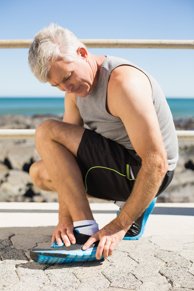 Fit man gripping his injured ankle on a sunny day-1