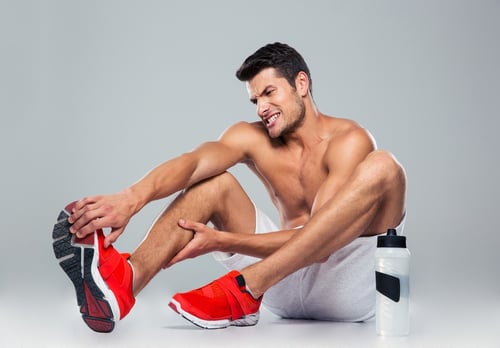 Portrait of a fitness man with foot pain over gray background.jpeg