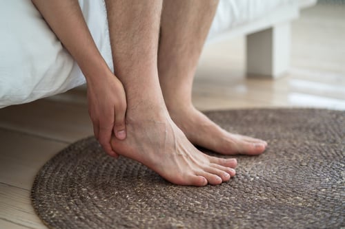 Man suffering from heel pain at home, sitting on side of bed